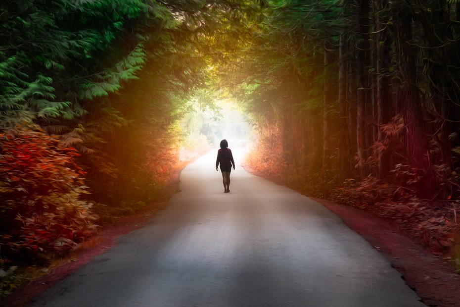 Person walking through dark heavily wooded path to light at the end.